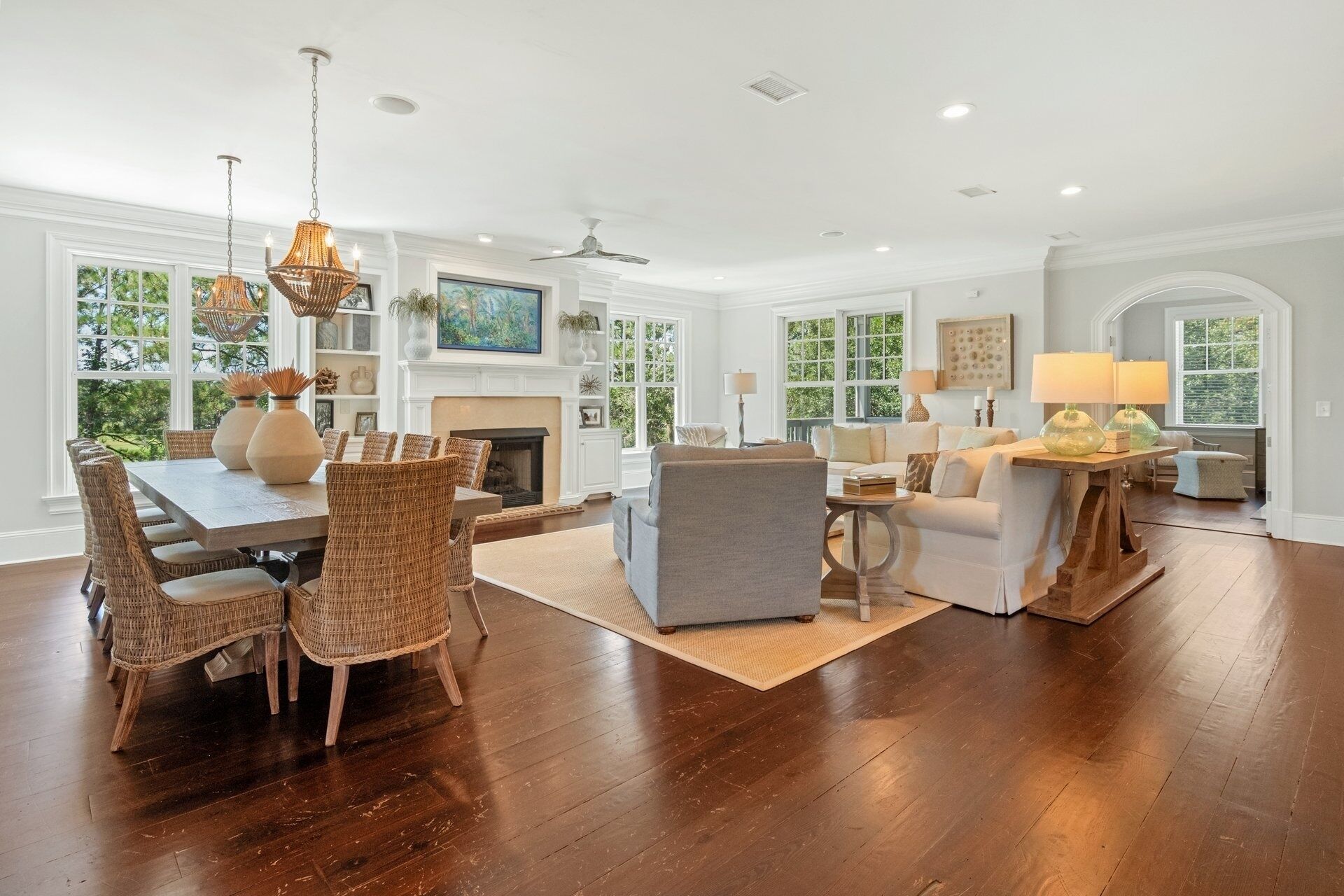 A spacious living room with a fireplace, large windows, and a dining area with wicker chairs.