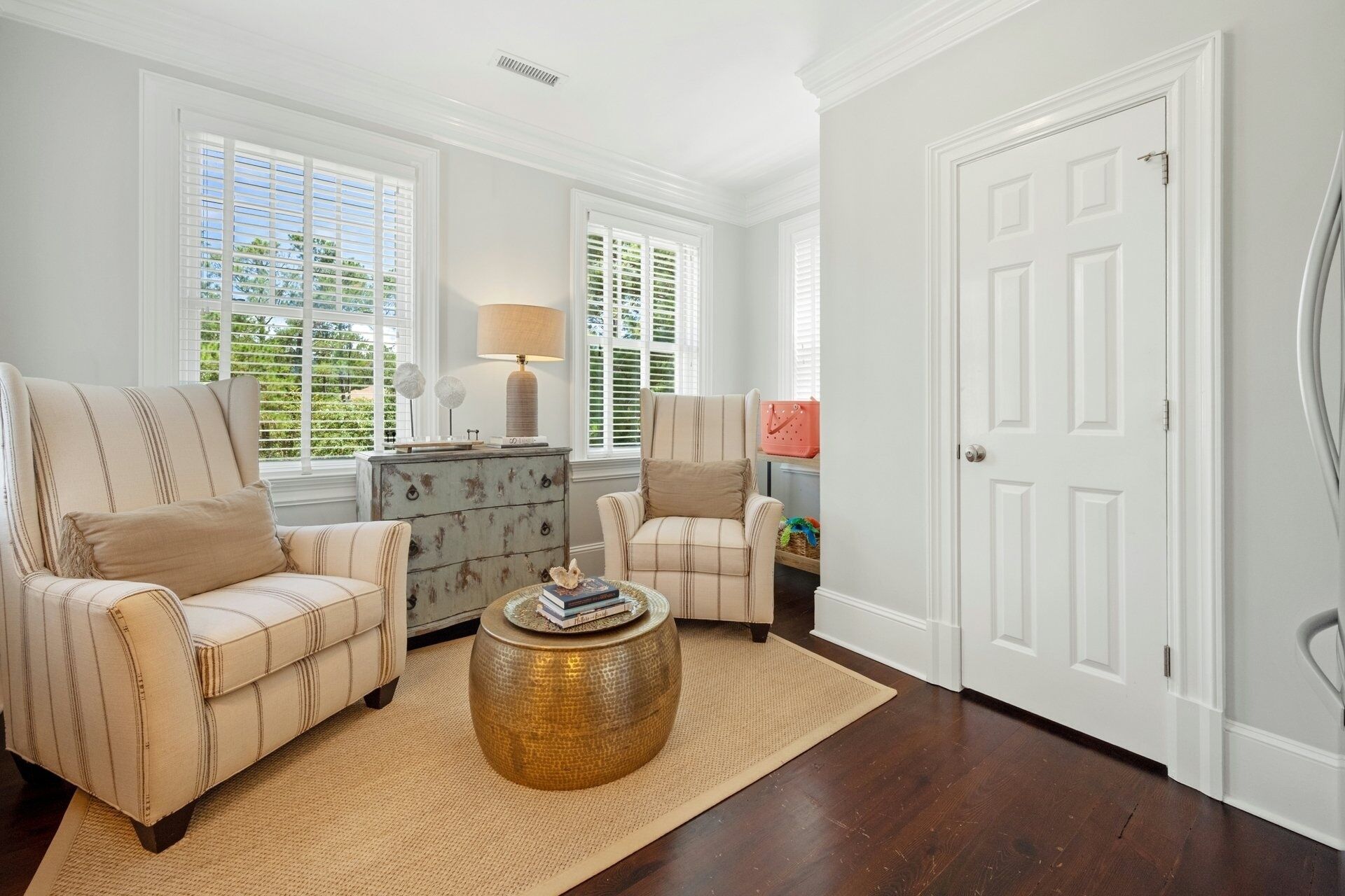 A living room with two striped armchairs, a wooden chest of drawers, a round coffee table, and a white door.