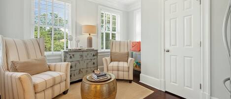 A living room with two striped armchairs, a wooden chest of drawers, a round coffee table, and a white door.