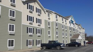 A multi-story hotel with a row of rooms on each floor, a parking lot with several vehicles, and a clear blue sky. - Value Place Louisville Ky South (Fairdale)