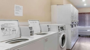 A laundry facility with multiple washing machines and dryers, a caution sign, and a note about not overfilling. - Value Place Louisville Ky South (Fairdale)