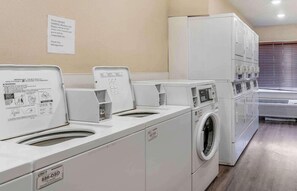 A laundry facility with multiple washing machines and dryers, a caution sign, and a note about not overfilling. - Value Place Louisville KY South (Fairdale)