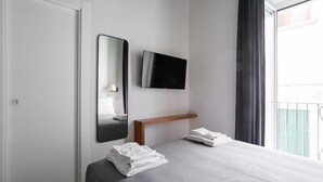 A hotel room with a bed, a TV mounted on the wall, a mirror, a bedside table, and a window with curtains. - Weaver Suite Apartment By Dimorra  (Naples)