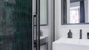 A modern bathroom with a white sink, a mirror, and a shower area with green tiles. - Weaver Suite Apartment By Dimorra  (Naples)