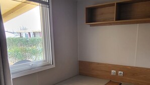 Une petite pièce avec un lit simple, une fenêtre et une étagère en bois.
