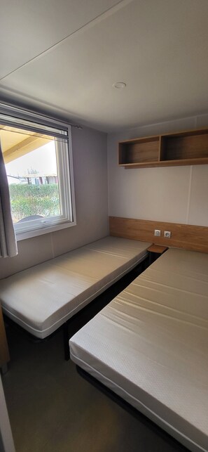 Ein kleines Zimmer mit einem Einzelbett, einem Fenster und einem Holzregal.