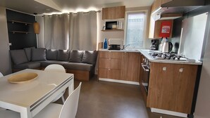 Une petite cuisine équipée avec une cuisinière, un four à micro-ondes et un évier. Une table à manger avec des chaises est placée devant un canap é gris.