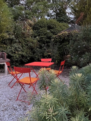 A patio with red metal chairs and a table, surrounded by dense greenery and trees. - La Grande Rossignol: Pool, spacious rooms, and private bathrooms in Occitanie. (Belvèze)