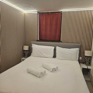 A hotel room with a bed, two nightstands, a lamp, a window with a red curtain, and a wooden wall paneling. - 5 minutes from St. Mark's Square (Venezia)