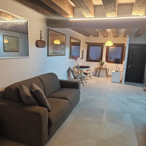 A living room with a sofa, a dining table with chairs, and a kitchen area with a refrigerator. - 5 minutes from St. Mark's Square (Venezia)