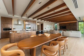 A modern kitchen with wooden cabinets, a large island, and a dining area with leather chairs. - Casa Chorotega, an Iconic Five-Bedroom Retreat in Peninsula Papagayo (Peninsula Papagayo)