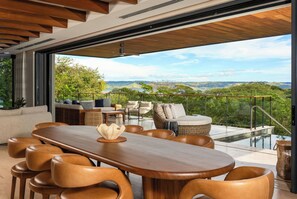 A modern outdoor dining area with a wooden table and leather chairs, overlooking a scenic landscape with a pool and a view of the hills. - Casa Chorotega, an Iconic Five-Bedroom Retreat in Peninsula Papagayo (Peninsula Papagayo)