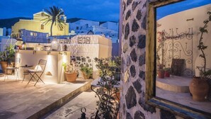 Un muro de piedra con una ventana, un balcón con sillas y plantas en macetas.