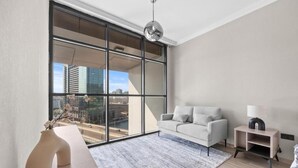 A modern living room with a large window, a sofa, a small table, and a lamp. - Bloomfields Luxurious 3Br in Al Maryah V (Abu Dhabi)