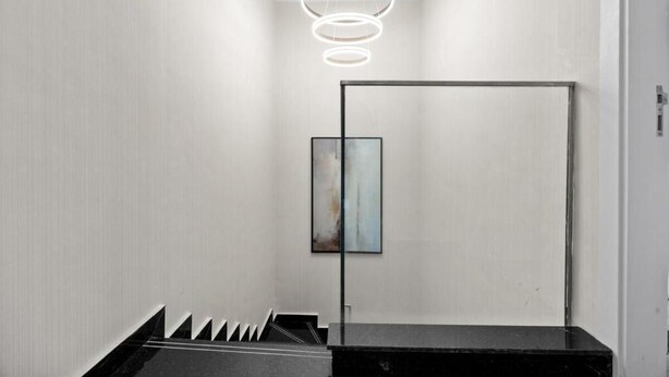 A modern interior with a minimalist design, featuring a black reception desk, a framed abstract painting, and a unique circular light fixture. - Bloomfields Luxurious 3Br in Al Maryah V (Abu Dhabi)