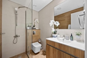 A modern bathroom with a glass shower enclosure, a white toilet, and a wooden vanity with a sink and mirror. - Bloomfields Luxurious 3Br in Al Maryah V (Abu Dhabi)