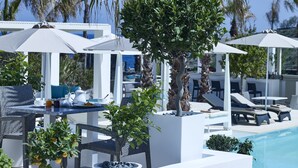Zona de piscina con sillones de descanso, sombrillas y una mesa con tetera y tazas.
