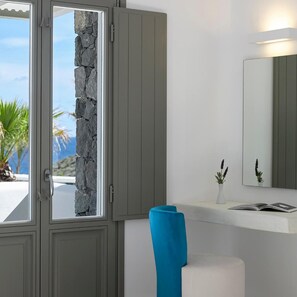 Una habitación con pared de piedra, un espejo, una silla azul y un banco blanco.