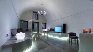A modern living room with a curved sofa, a coffee table, and a TV. - Nefeli Homes (Santorini)