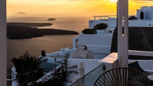 A terrace with a view of the sea and sunset, featuring white architecture, a table, and chairs. - Nefeli Homes (Santorini)