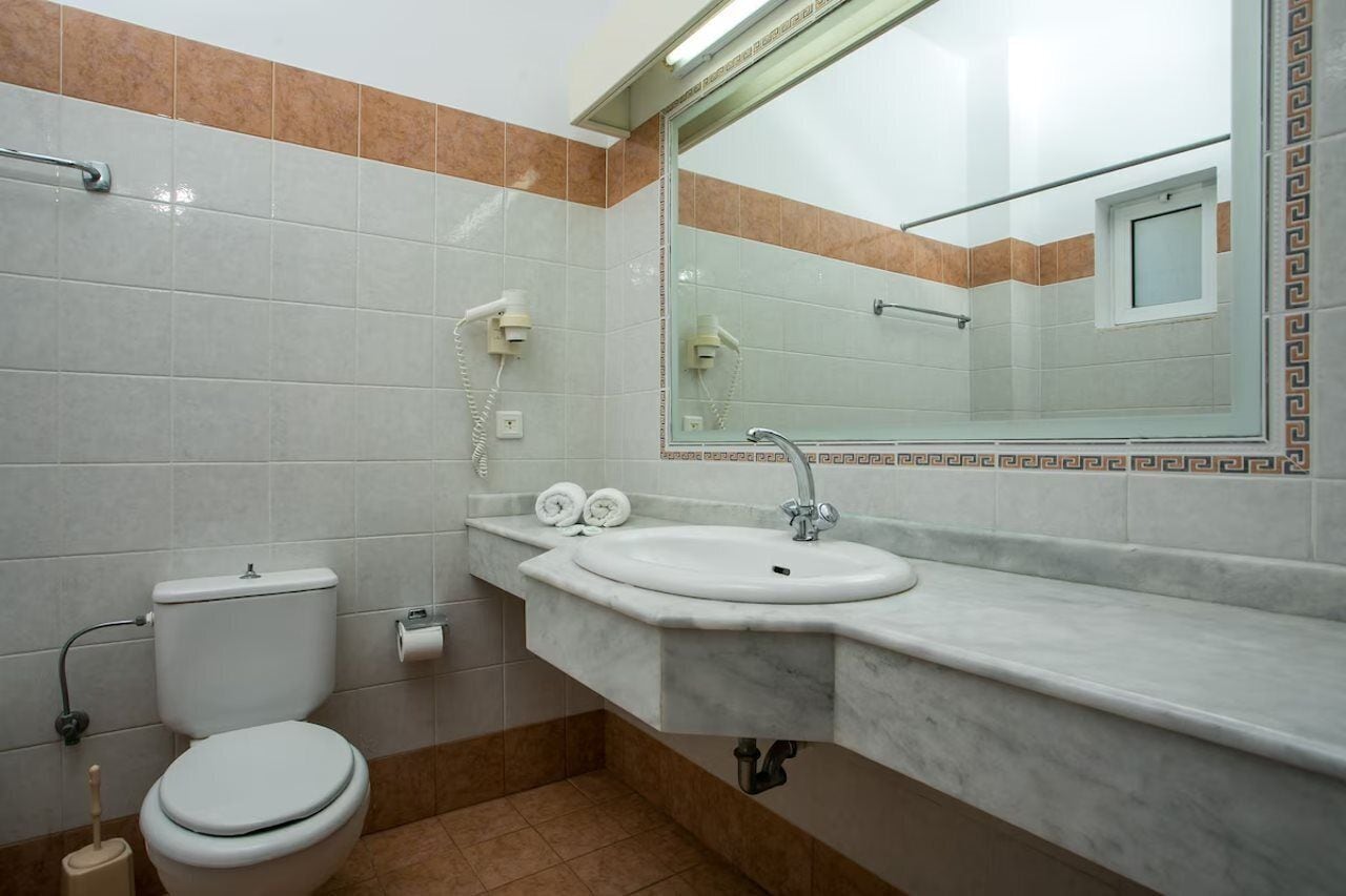 A bathroom with a toilet, sink, and mirror.
