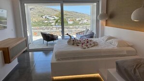 Un dormitorio moderno con una cama grande, una zona de estar con una silla y vistas a una ladera a través de un ventanal corredero.