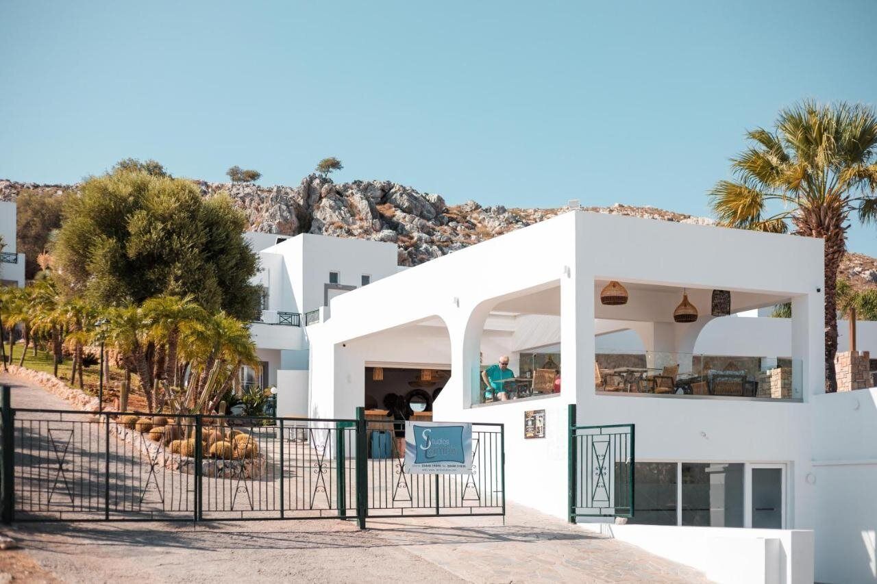 A white building with a covered outdoor seating area, a gated entrance, and a view of a rocky hillside.