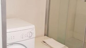 Une salle de bain moderne et compacte, avec une machine à laver blanche et une petite serviette posée sur le comptoir.
