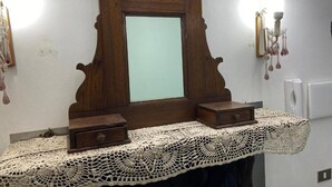 Une coiffeuse en bois avec un miroir, deux tiroirs et un chemin de table en dentelle.