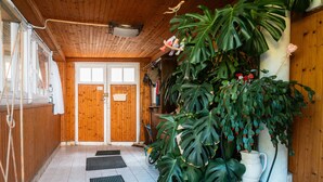 Un interior de madera con una planta grande en maceta, una puerta blanca y un suelo de baldosas.