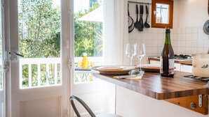 Una cocina con encimera de madera, una botella, dos vasos y una ventana con vistas a la vegetación.