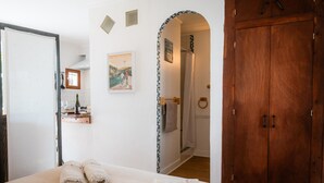 Un dormitorio con cama, armario de madera, baño con ducha y estante con artículos de aseo.