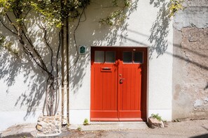 A red door with a window, a stone base, and a sign on the wall. - Gîte l'inattendue - Accueil Vélo Certified (Courseulles-sur-Mer)