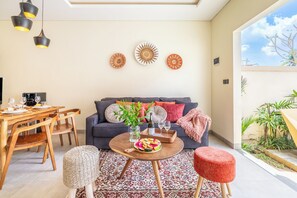 A modern living room with a dining area, a sofa with cushions, a coffee machine, and decorative plates on the wall. - Solari Elephant Villa (Ubud)