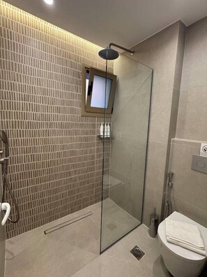 Un baño moderno con cabina de ducha de vidrio, inodoro y un pequeño estante con artículos de aseo.