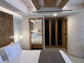 A modern bedroom with a bed, wooden wardrobe, and a mirror. - The Noverian Antama Organic Beach Resort Chania (Chania)
