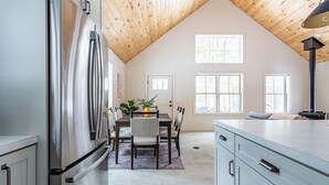 A kitchen with a stainless steel refrigerator, wooden ceiling, and a dining area with a table and chairs. - Lakefront with Private Dock & Canoe Kenoza Den (Jeffersonville)