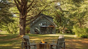 A cabin with a fire pit and two Adirondack chairs in a forested area. - Lakefront with Private Dock & Canoe Kenoza Den (Jeffersonville)