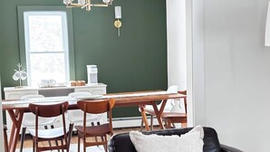 A dining area with a wooden table and chairs, a black leather couch with a white pillow, and a green accent wall. - Kenoza House with Private Lake and Kayaks (Callicoon)