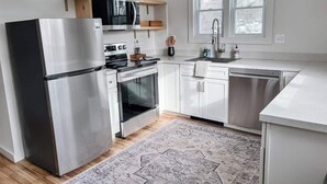 A modern kitchen with stainless steel appliances, white cabinetry, a wooden shelf, and a patterned rug. - Kenoza House with Private Lake and Kayaks (Callicoon)