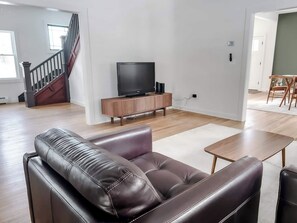 Un salon moderne avec un canapé en cuir, un meuble de rangement en bois et un téléviseur.