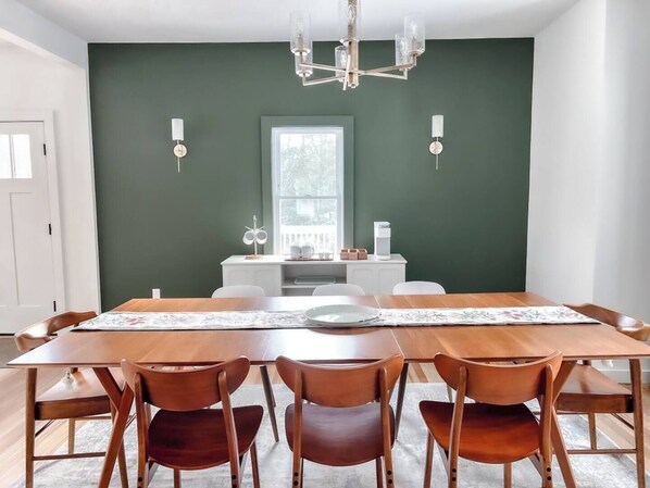 Un coin repas avec une table en bois et quatre chaises, un lustre et une fenêtre donnant sur les arbres.