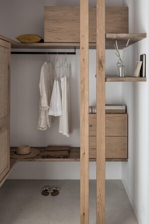 A room with a wooden wardrobe, a shelf with decorative items, and a hanging rack with clothes. - A Hotel Mykonos (Mykonos)