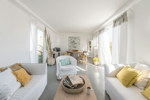 Amplia sala de estar con sofá, sillón y mesa de centro, además de un comedor y vistas al exterior.