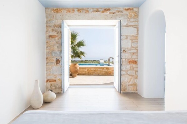 A room with a stone wall and a view of a pool and palm tree. - Calme Boutique Hotel Paros (Paros)