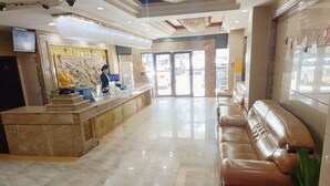 Een hotel lobby met een receptiebalie, een zithoek en een groot raam.