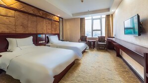 Een hotelkamer met twee bedden, een bureau, een stoel, een televisie en een raam met gordijnen.