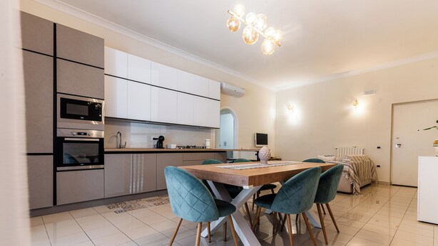 A modern kitchen with built-in appliances, a dining area with teal chairs, and a chandelier. - Cozy and modern apartment in the most elegant neighborhood of Naples (Napoli)