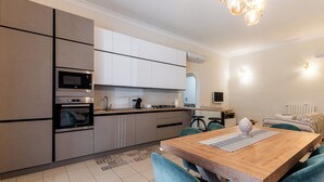 A modern kitchen with built-in appliances, a dining area with a wooden table and teal chairs, and a visible island with a kettle. - Cozy and modern apartment in the most elegant neighborhood of Naples (Napoli)