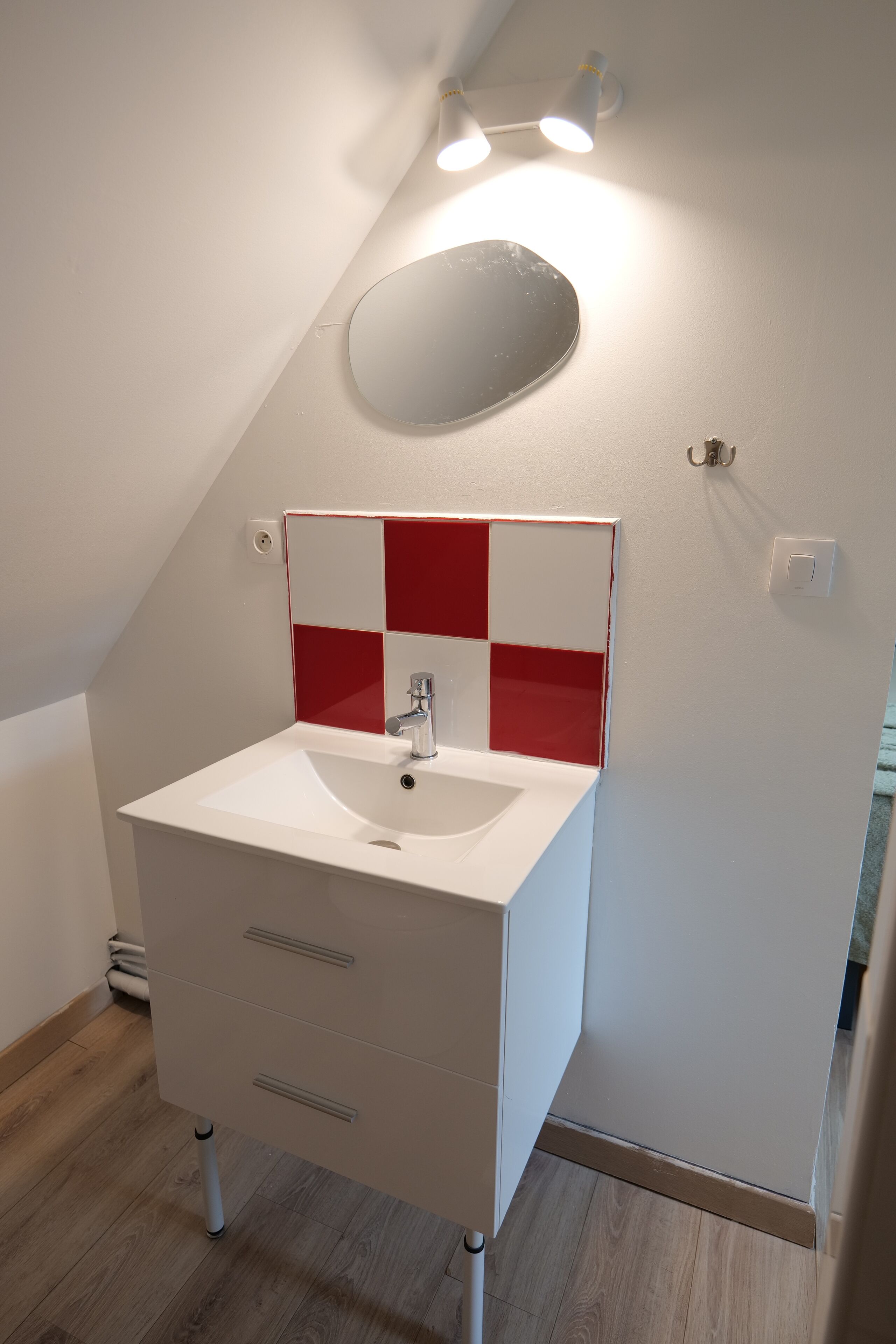 A bathroom with a white sink, red and white tiled backsplash, and a mirror.